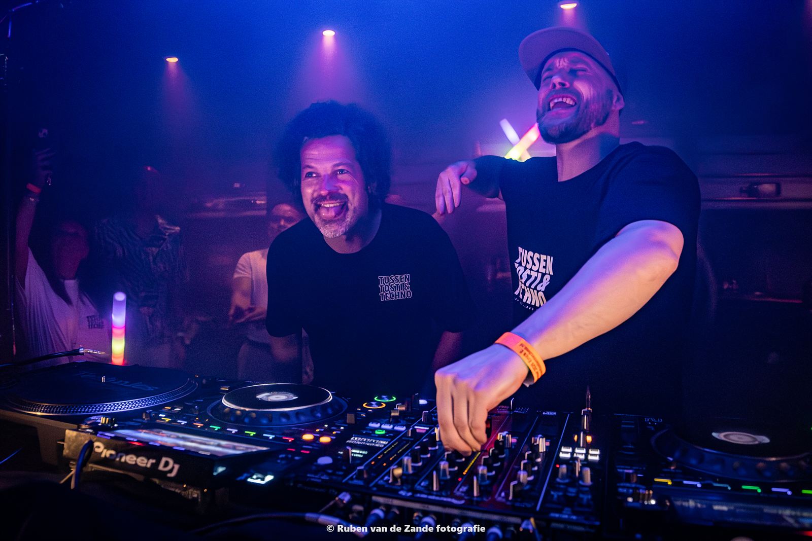 Dj achter de draaitafels in groen licht, met publiek eromheen